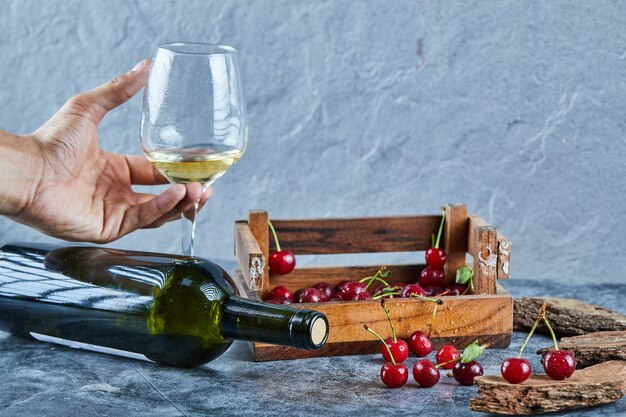 Frau, die ein Glas Weißwein und Holzkiste der Kirschen auf blauer Oberfläche hält