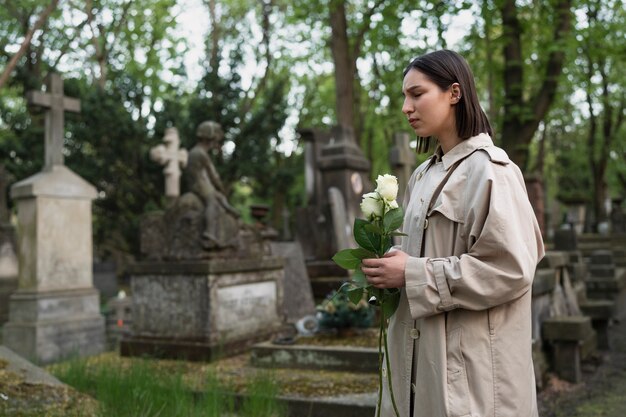 Frau, die ein Grab auf dem Friedhof besucht und Blumen bringt