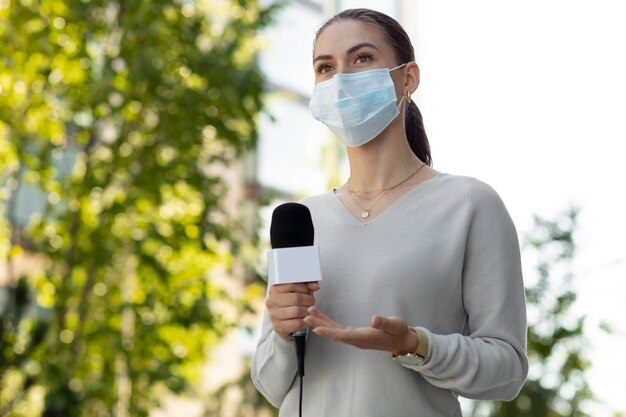 Frau, die ein Mikrofon hält, während sie eine medizinische Maske trägt