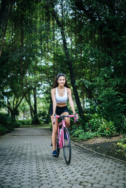 Frau, die ein Rennrad im Park reitet. Portrait der jungen schönen Frau auf rosafarbenem Fahrrad.