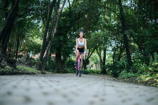 Frau, die ein Rennrad im Park reitet. Portrait der jungen schönen Frau auf rosafarbenem Fahrrad.