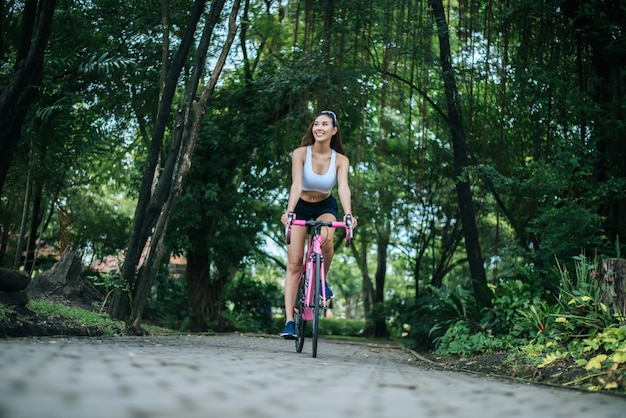 Frau, die ein Rennrad im Park reitet. Portrait der jungen schönen Frau auf rosafarbenem Fahrrad.