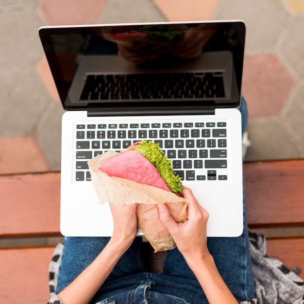 Kostenloses Foto frau, die ein sandwich vor laptop hält