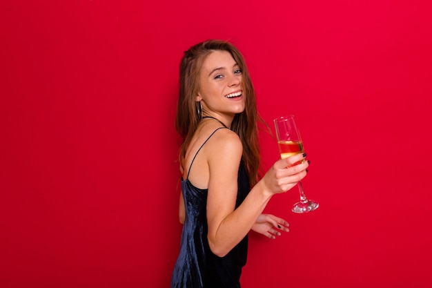 Frau, die ein schwarzes Kleid trägt und ein Champagnerglas hält, das auf Rot aufwirft