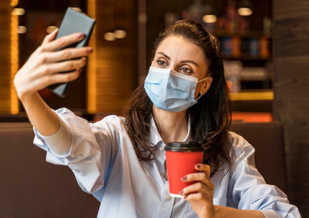 Frau, die ein Selfie in einem Restaurant beim Tragen einer Gesichtsmaske nimmt