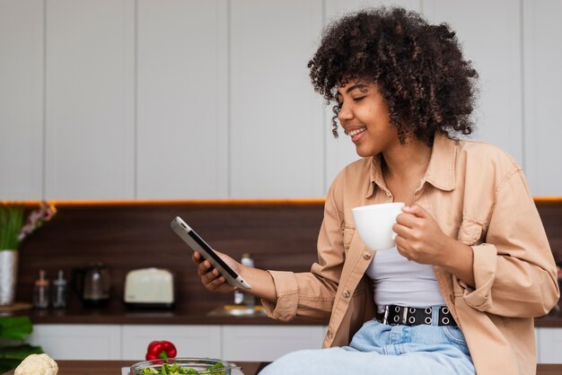 Frau, die ein Telefon und einen Tasse Kaffee in der Küche hält