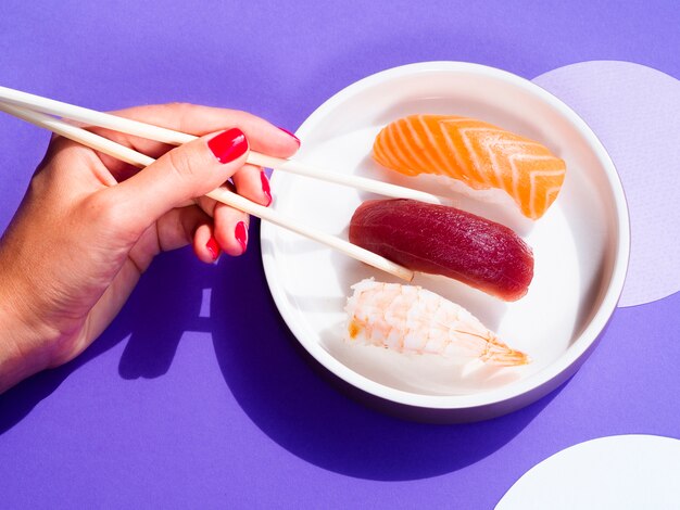 Frau, die ein Thunfischsushi von einer weißen Schüssel mit Sushi nimmt