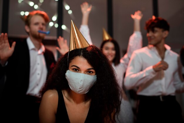 Frau, die eine medizinische Maske neben ihren Freunden auf Silvesterparty trägt