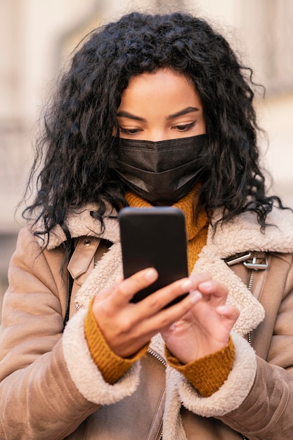 Kostenloses Foto frau, die eine medizinische maske trägt, während sie ihr telefon überprüft