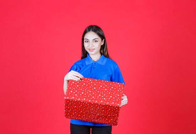 Frau, die eine rote Geschenkbox mit weißen Punkten darauf hält.