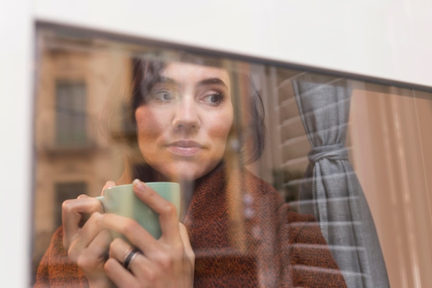 Kostenloses Foto frau, die eine tasse kaffee hält, während draußen schaut