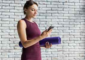 Kostenloses Foto frau, die eine yogamatte bei der stellung an ihrem telefon hält