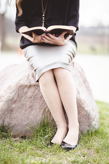 Frau, die einen grauen Rock trägt und ein Buch liest, während sie auf einem Felsen sitzt