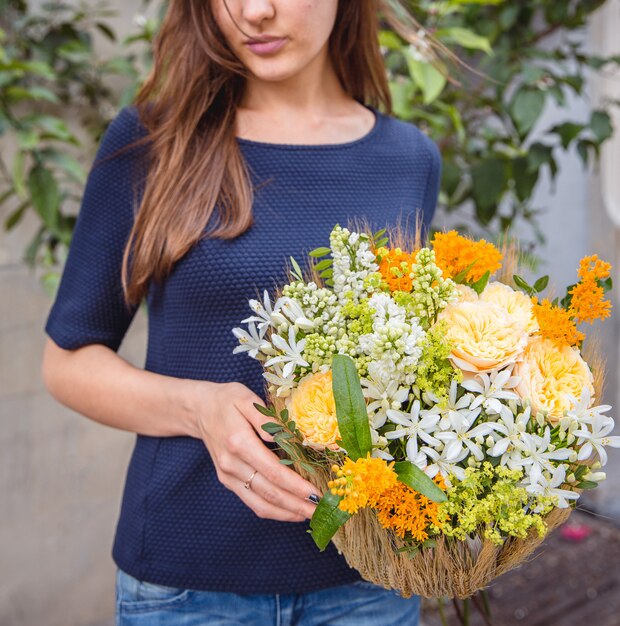 Frau, die einen Korb der gelben und weißen Blumen anhält.