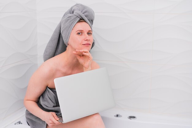 Frau, die einen Laptop in der Badewanne hält