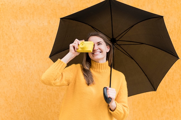 Frau, die einen schwarzen Regenschirm und eine gelbe Kamera hält