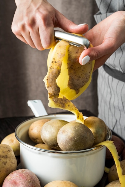 Frau, die einige rohe Kartoffeln Nahaufnahme schält