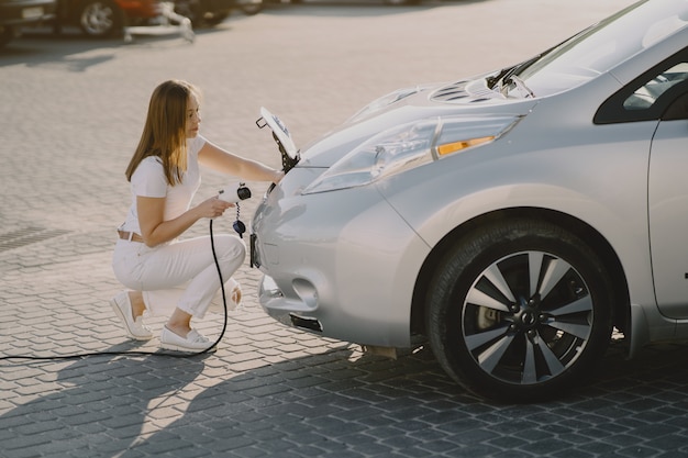 Frau, die Elektroauto an der elektrischen Tankstelle auflädt