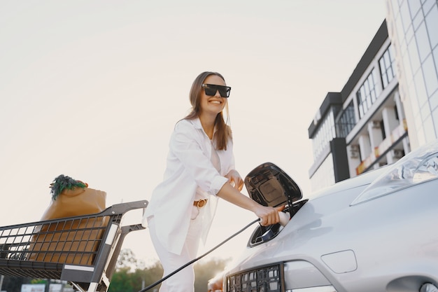 Frau, die Elektroauto an der elektrischen Tankstelle auflädt