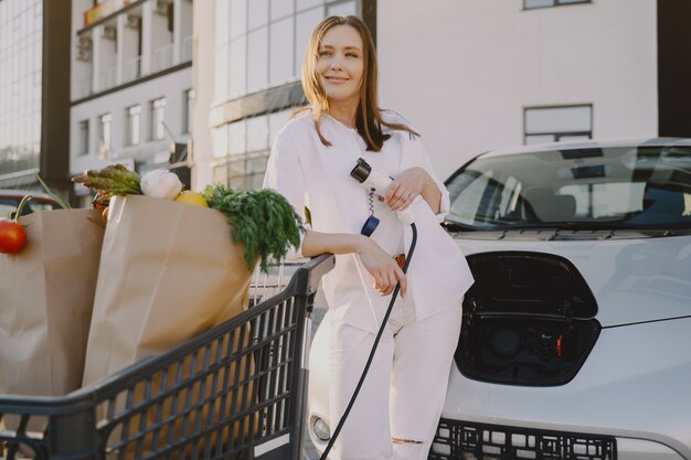 Frau, die Elektroauto an der elektrischen Tankstelle auflädt