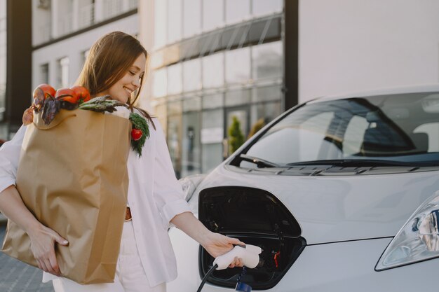 Frau, die Elektroauto an der elektrischen Tankstelle auflädt