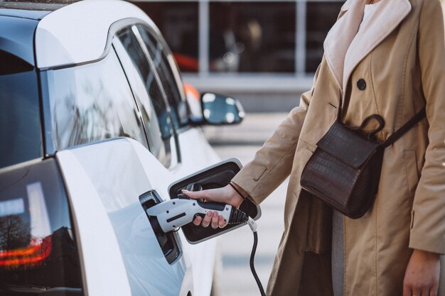 Frau, die Elektroauto an der elektrischen Tankstelle auflädt