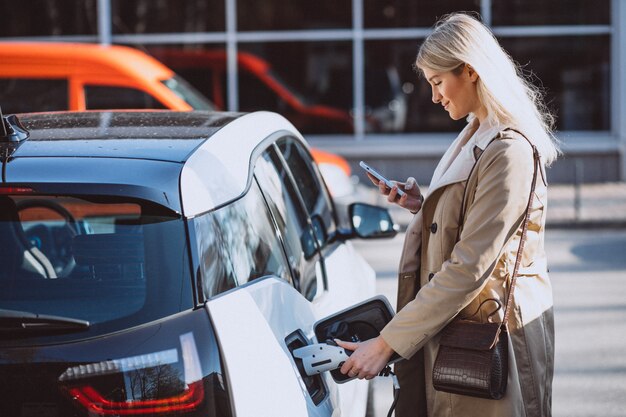 Frau, die Elektroauto an der elektrischen Tankstelle auflädt