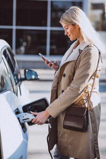 Frau, die Elektroauto an der elektrischen Tankstelle auflädt