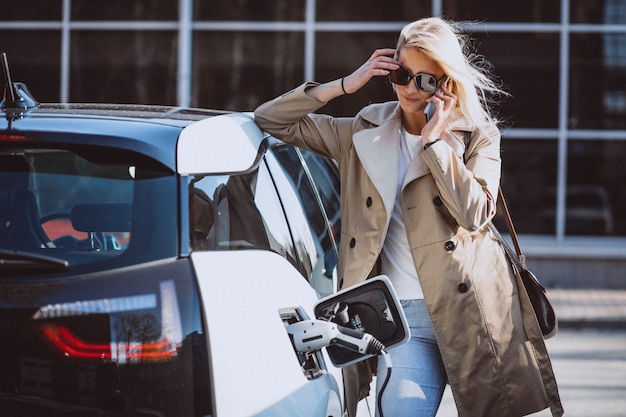 Frau, die Elektroauto an der elektrischen Tankstelle auflädt