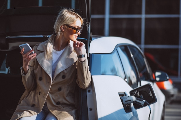 Frau, die Elektroauto an der elektrischen Tankstelle auflädt