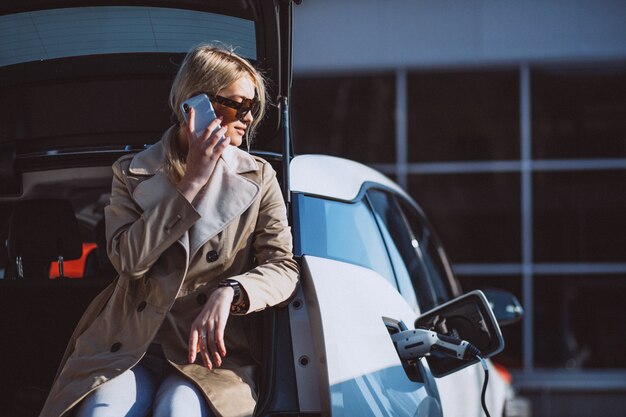 Frau, die Elektroauto an der elektrischen Tankstelle auflädt