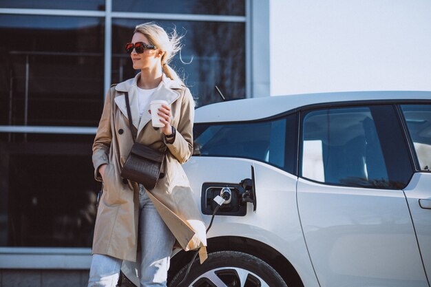 Frau, die Elektroauto an der elektrischen Tankstelle auflädt