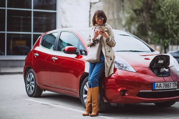 Frau, die elektroauto an der elektrischen tankstelle auflädt