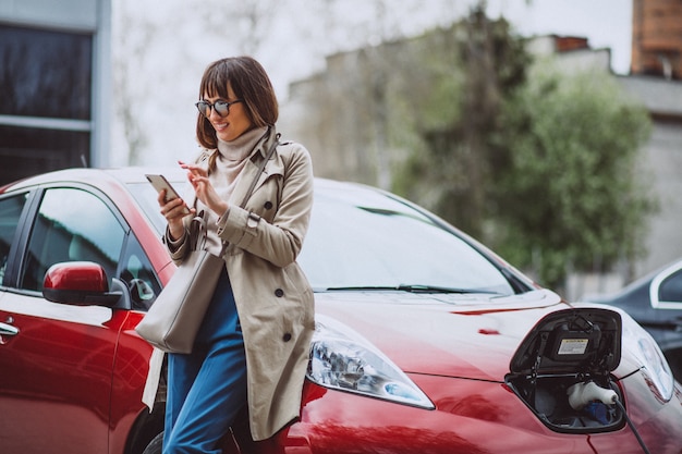 Frau, die Elektroauto an der elektrischen Tankstelle auflädt