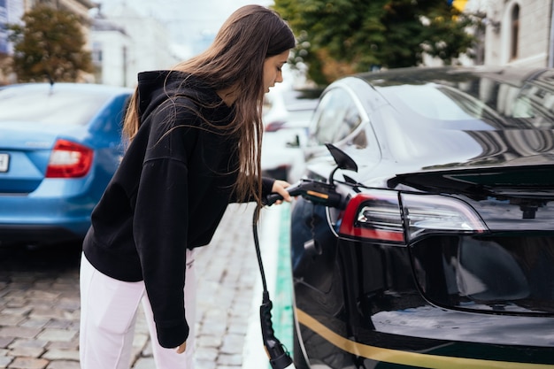 Frau, die Elektroauto an der Ladestation auflädt.