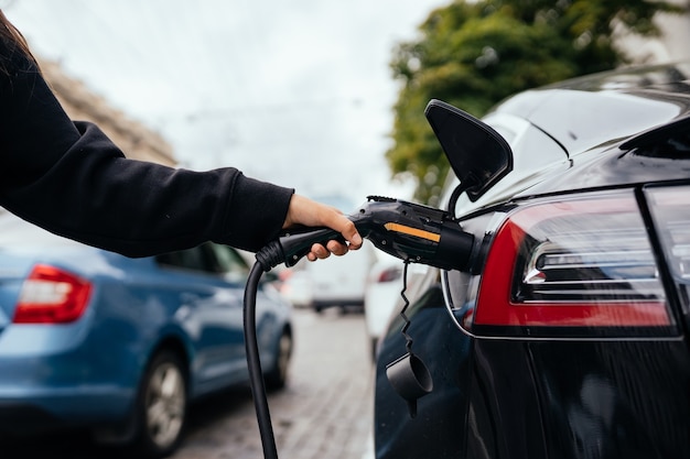 Frau, die Elektroauto an der Ladestation auflädt.