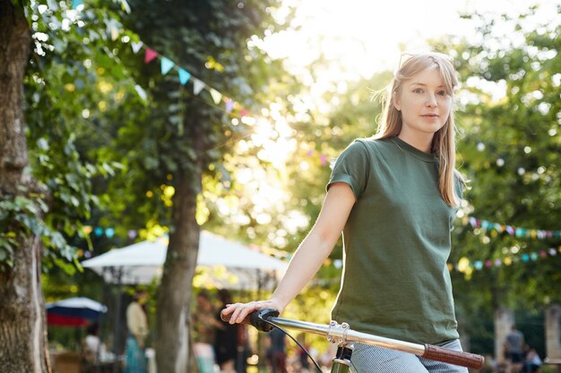 Frau, die Fahrrad fährt. Porträt der jungen Frau, die auf einem Fahrrad sitzt, verwirrt und lächelnd in einem Stadtpark