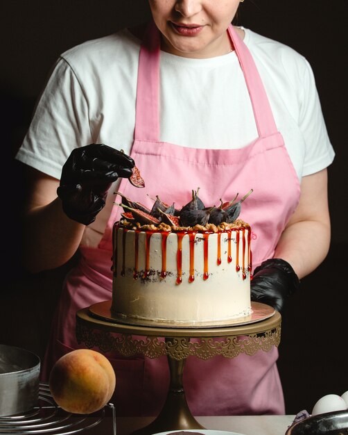 Frau, die Feigenstück auf klassischem Kuchen hinzufügt, verziert mit Feigen und Sirup