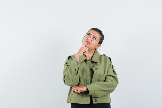 Frau, die Finger auf Kinn in Jacke, T-Shirt hält und nachdenklich aussieht