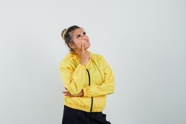 Frau, die Finger auf Wange im Sportanzug hält und nachdenklich, Vorderansicht schaut.