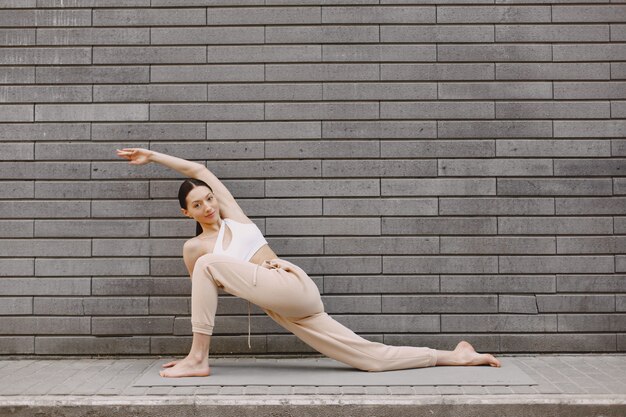 Frau, die fortgeschrittenes Yoga gegen eine dunkle Stadtmauer praktiziert