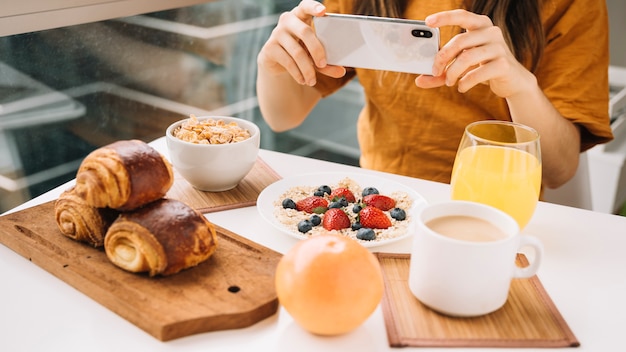 Frau, die Foto des Frühstücks am weißen Tisch macht