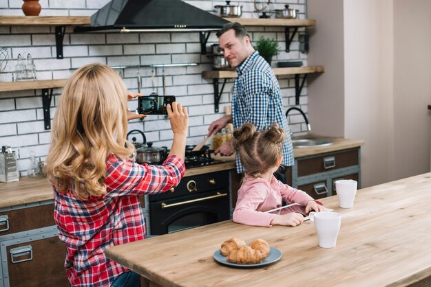 Kostenloses Foto frau, die foto ihres ehemanns im handy beim kochen in der küche macht