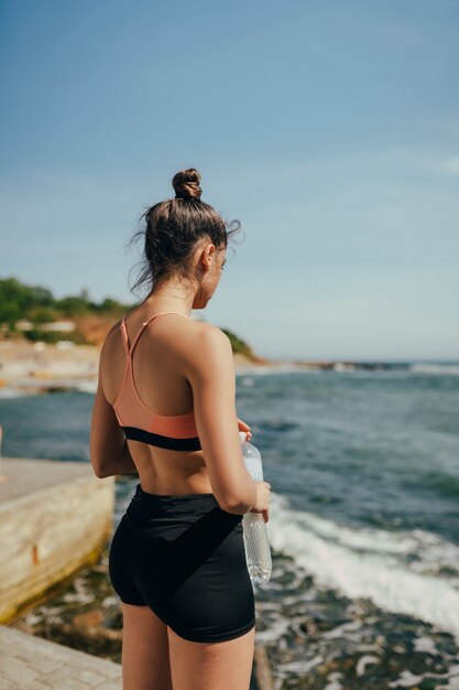 Frau, die frisches Wasser von der Flasche nach dem Training am Strand trinkt