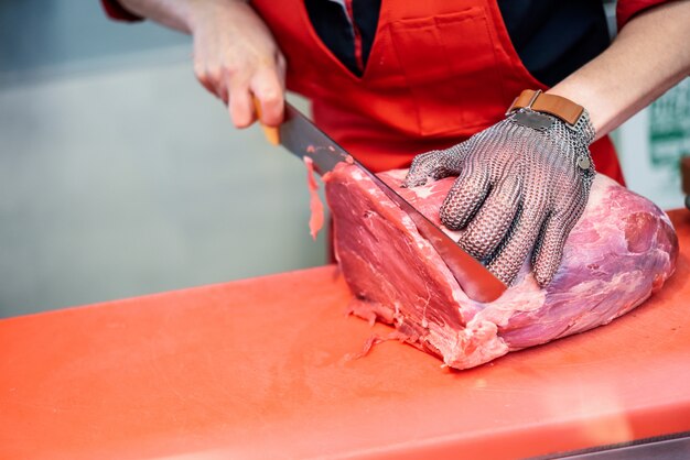 Frau, die Frischfleisch in einer Metzgerei mit Metallsicherheitsmaschenhandschuh schneidet