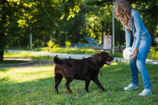 Frau, die Fußball mit ihrem Hund im Garten spielt