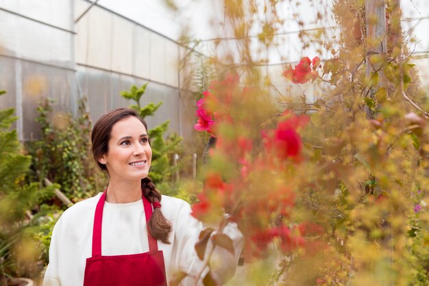 Frau, die Gartenarbeitkleidung trägt und Blumen im Gewächshaus bewundert