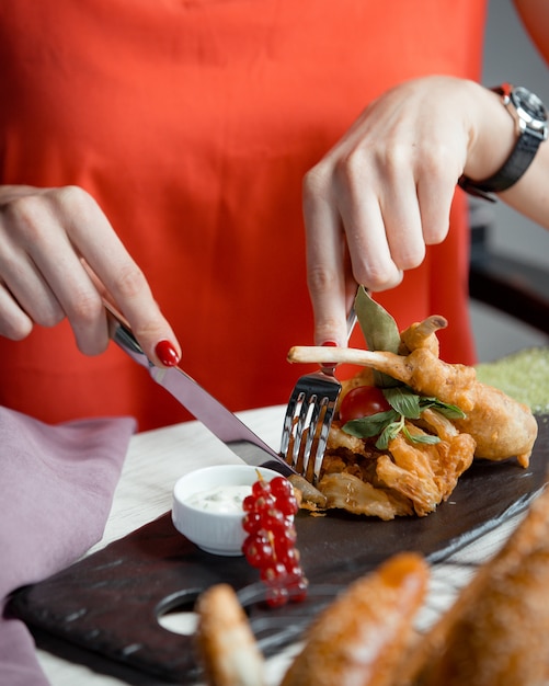 Frau, die gebratenes gegrilltes Huhn mit Gabel und Messer schneidet