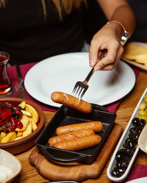 Frau, die gegrillte Würste von der kleinen Gusseisenpfanne nimmt