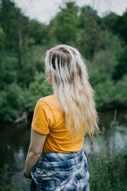 Kostenloses Foto frau, die gelbes hemd mit blauer und weißer jacke trägt, die auf dem hintergrund der bäume steht